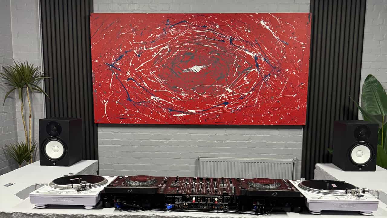 The DJ room square-on: two AlphaTheta CDJ-3000X players either side of a Pioneer DJ DJM-A9 with a white Reloop RP-7000 turntable at each end, Yamaha HS8 monitors on the wings of a hand-built concrete booth, beneath a red and white abstract canvas