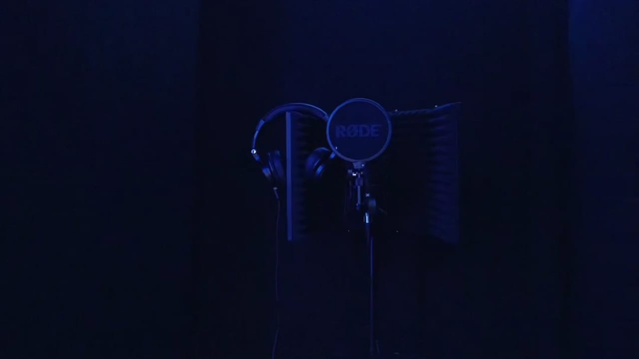 The music studio lit by violet LED strips, with the desk, monitors and vocal booth.